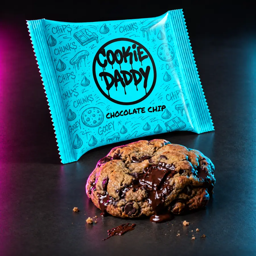 Neon cyan Cookie Daddy wrapper, black ring tag with CHOCOLATE CHIP printed under it, unwrapped chocolate chip cookie in front on dark concrete