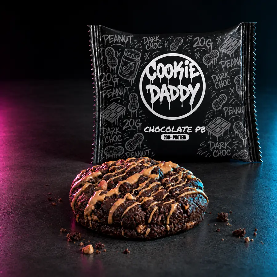 Matte black Cookie Daddy wrapper, black ring tag with CHOCOLATE PB printed under it, unwrapped chocolate pb cookie in front on dark concrete