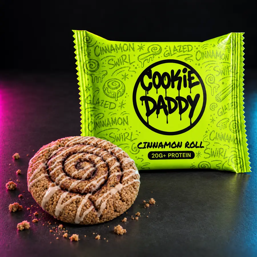 Acid lime Cookie Daddy wrapper, black ring tag with CINNAMON ROLL printed under it, unwrapped cinnamon roll cookie in front on dark concrete