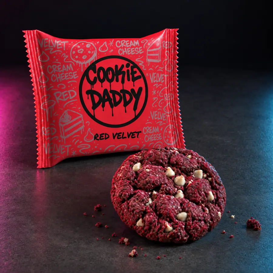 Neon red Cookie Daddy wrapper, black ring tag with RED VELVET printed under it, unwrapped red velvet cookie in front on dark concrete
